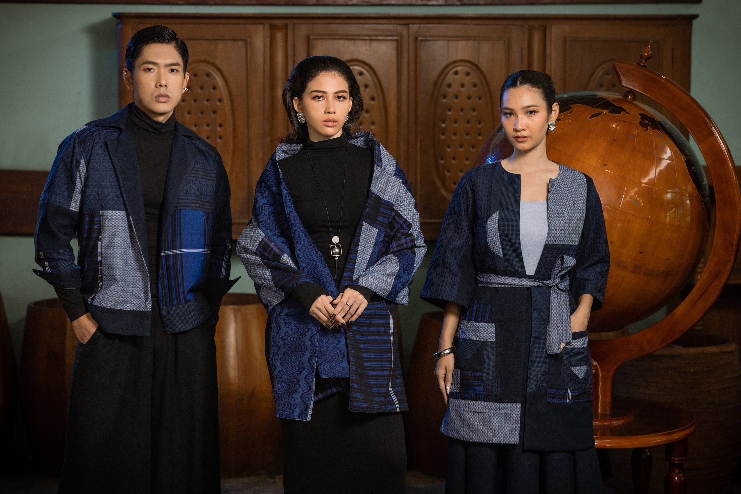 Three models in blue patchwork jackets from New Traditional, in a room with an antique globe